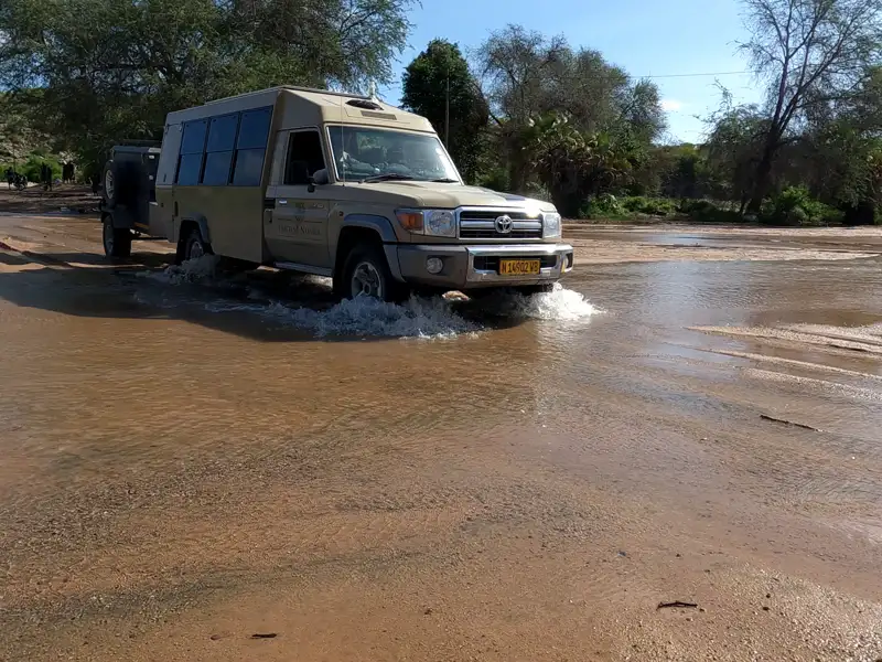 Safari-Fahrzeug durchquert ein Gewässer, Hinweis auf mögliche Flussdurchquerungen oder Fahrten durch überflutete Gebiete während der Safari.