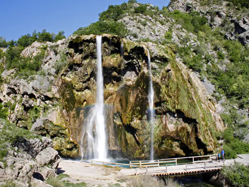 Szenerischer Wasserfall mit einem Holzsteg im Vordergrund.