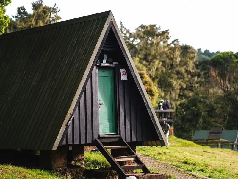 Einfache Berghütte mit A-förmigem Dach und grüner Tür, wahrscheinlich eine Unterkunft auf der Reise.