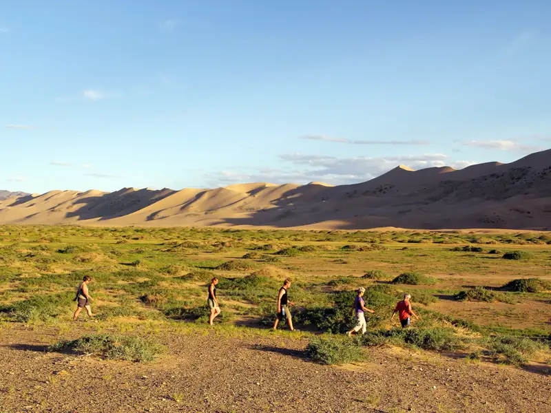 Wanderer in einer Wüstenlandschaft mit Sanddünen im Hintergrund.