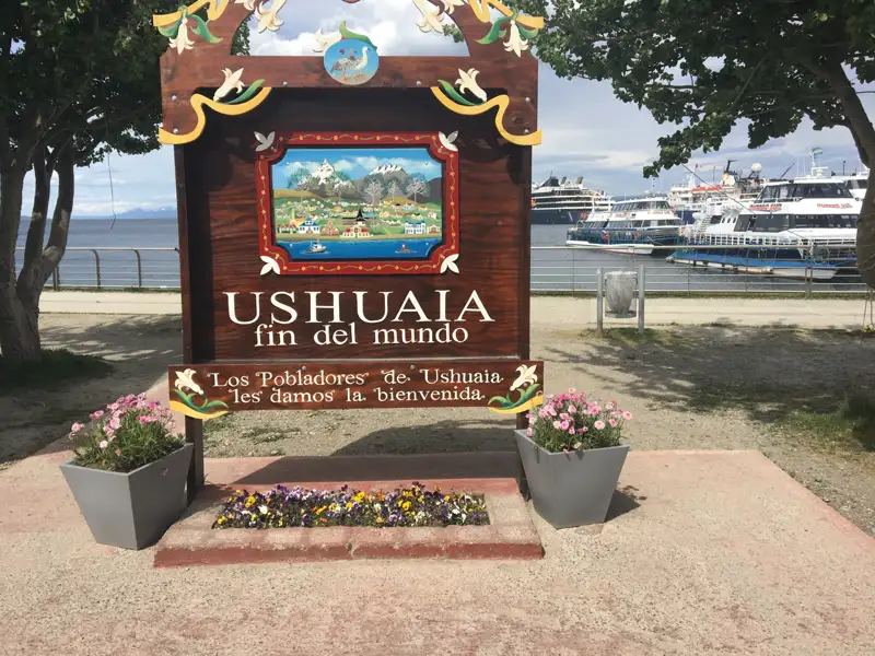 Willkommensschild in Ushuaia, Argentinien, mit dem Schriftzug 'Ende der Welt' und Blick auf den Hafen.