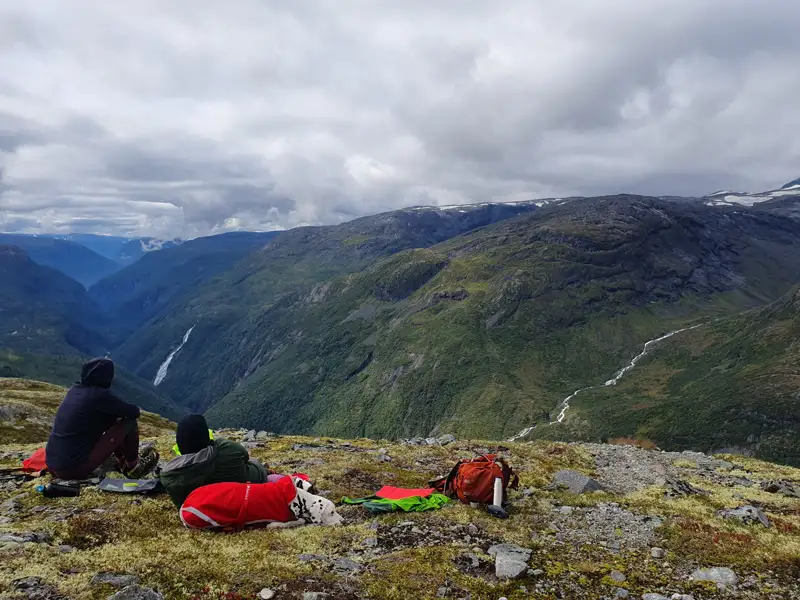 Wanderer machen eine Pause und bewundern die Aussicht auf das Tal, einen Wasserfall und die umliegenden Berge.