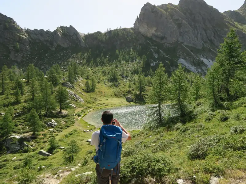 Wanderer fotografiert Bergsee inmitten einer alpinen Landschaft.