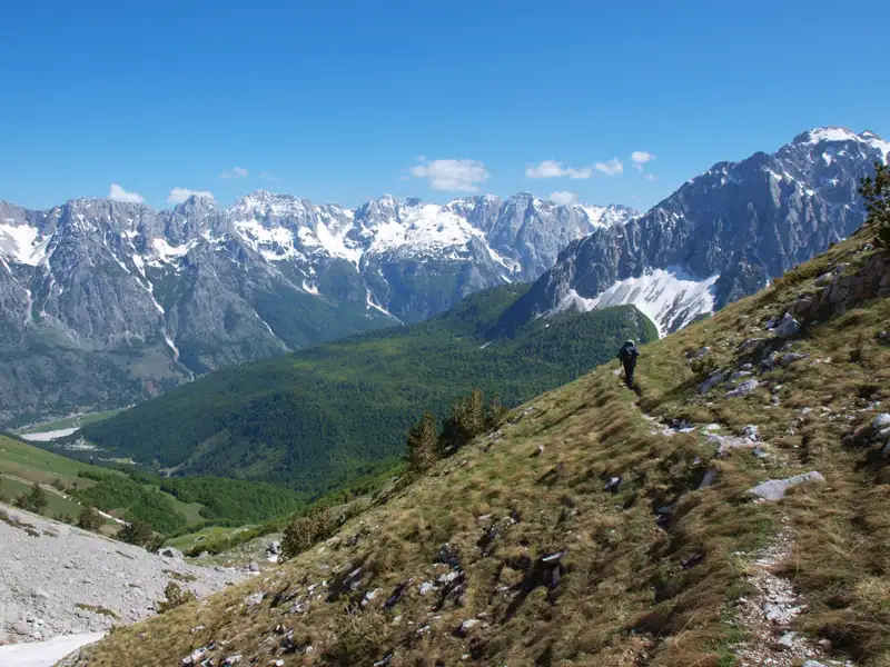 Wanderer auf einem Bergpfad inmitten einer beeindruckenden Bergkulisse mit schneebedeckten Gipfeln.