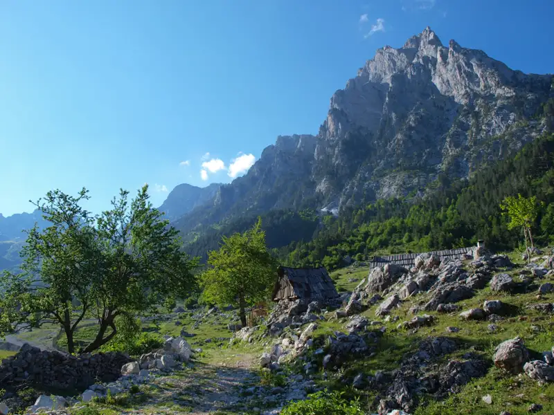 Eine einfache Berghütte in einer bergigen Landschaft mit einem hohen Gipfel im Hintergrund.