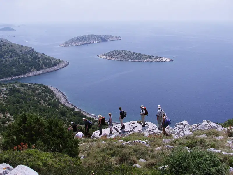 Wandergruppe auf einem Küstenpfad mit Blick auf das Meer und vorgelagerte Inseln.