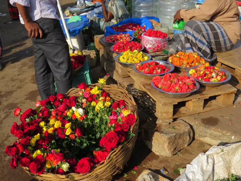 Rosen in verschiedenen Farben werden auf einem Markt in Schalen und einem großen Korb angeboten.