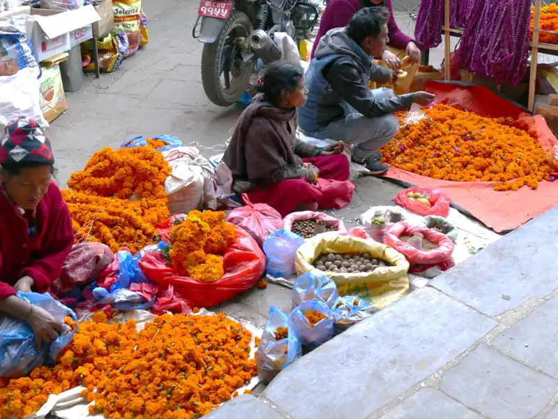 Marktstand mit orangenen Ringelblumen und anderen Waren, betreut von Frauen.