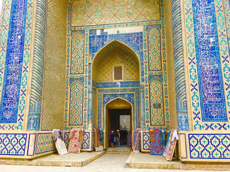 Eingang eines Gebäudes mit detaillierten Mosaiken und ausgestellten Teppichen.