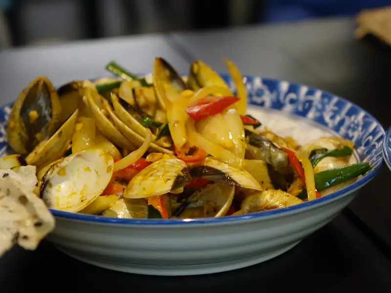 Gebratene Venusmuscheln, angerichtet mit Zwiebeln, Paprika und Frühlingszwiebeln.