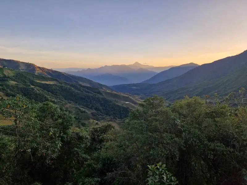 Sonnenuntergang über einem bewaldeten Tal und Bergen.