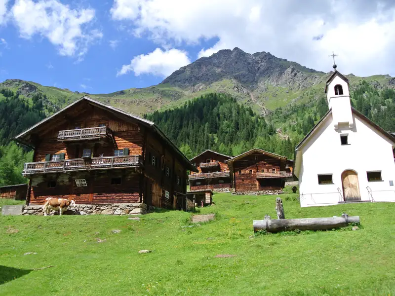Traditionelle Holzhäuser und eine Kapelle in einer Berglandschaft.