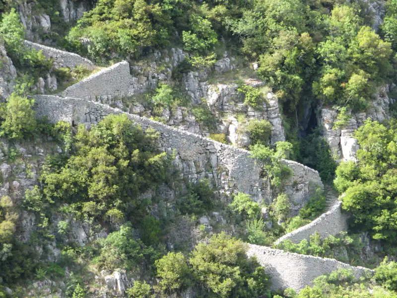 Historische Steinmauern in einer bewaldeten Berglandschaft.