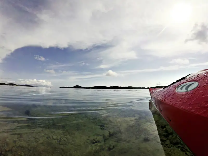 Rotes Kajak im ruhigen Wasser mit Inseln im Hintergrund.