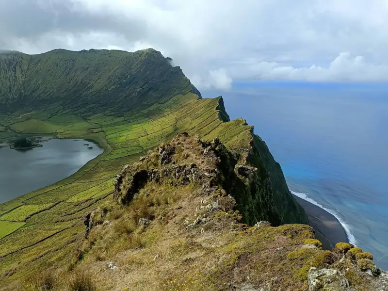Spektakulärer Blick auf einen Kratersee, umgeben von grünen Feldern, der an einer steilen Klippe zum Meer hin abfällt.