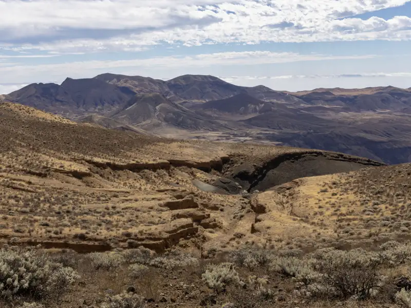 Ausblick auf eine trockene, bergige Landschaft mit spärlicher Vegetation und tiefen Schluchten.
