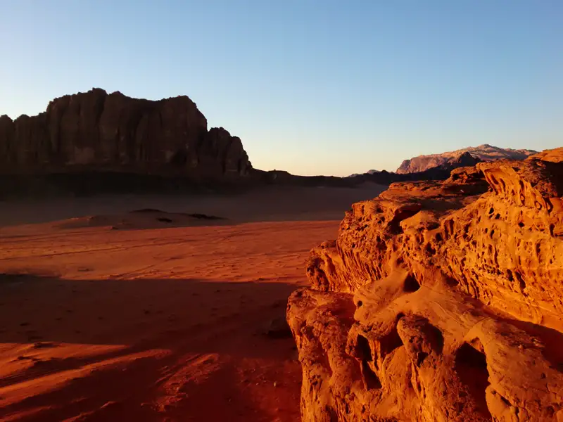 Roter Sand und Felsformationen in der Wüste bei Sonnenuntergang.