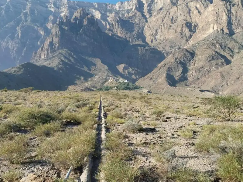 Pipeline in einer wüstenartigen Landschaft mit Bergen im Hintergrund.