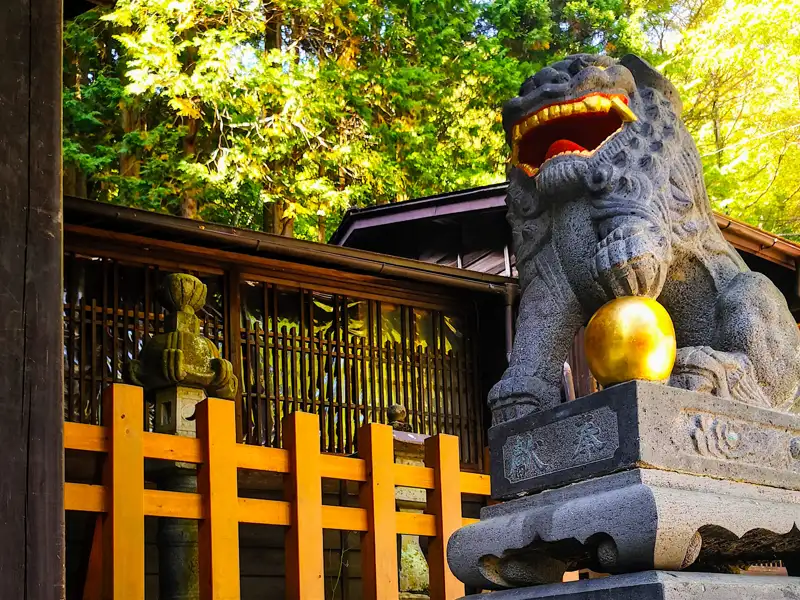 Steinerner Löwe mit goldener Kugel am Eingang eines traditionellen japanischen Gebäudes.
