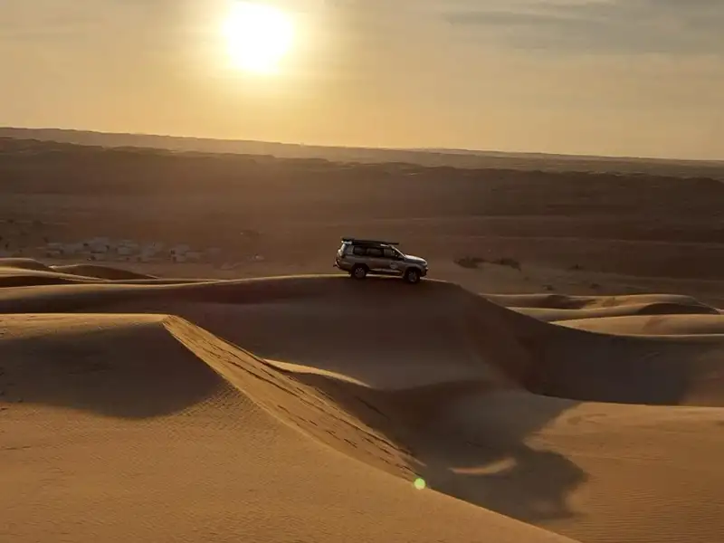 Geländewagen auf einer Düne im Sonnenuntergang.