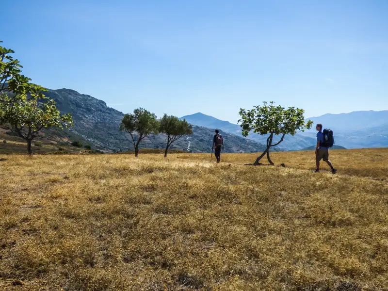 Zwei Wanderer mit Rucksäcken auf einer Wanderung durch eine trockene, bergige Landschaft.