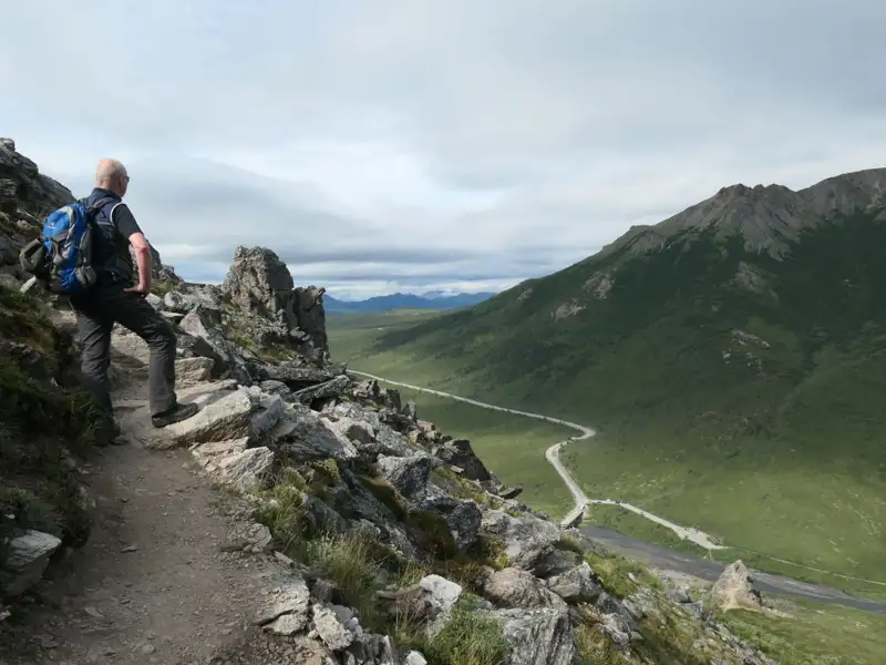 Wanderer auf einem Bergpfad mit Blick auf ein Tal und eine Straße.