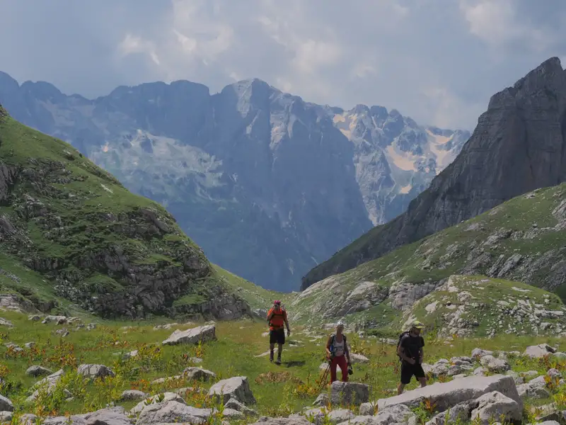 Drei Wanderer auf einem Bergpfad mit Blick auf die schneebedeckten Gipfel.