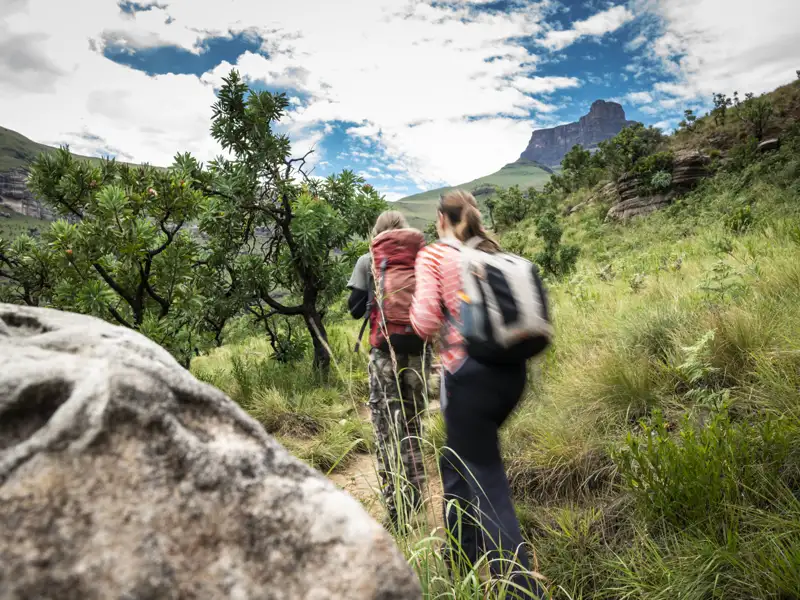Zwei Wanderer auf einem Bergpfad. Im Hintergrund ist ein Berg zu sehen.