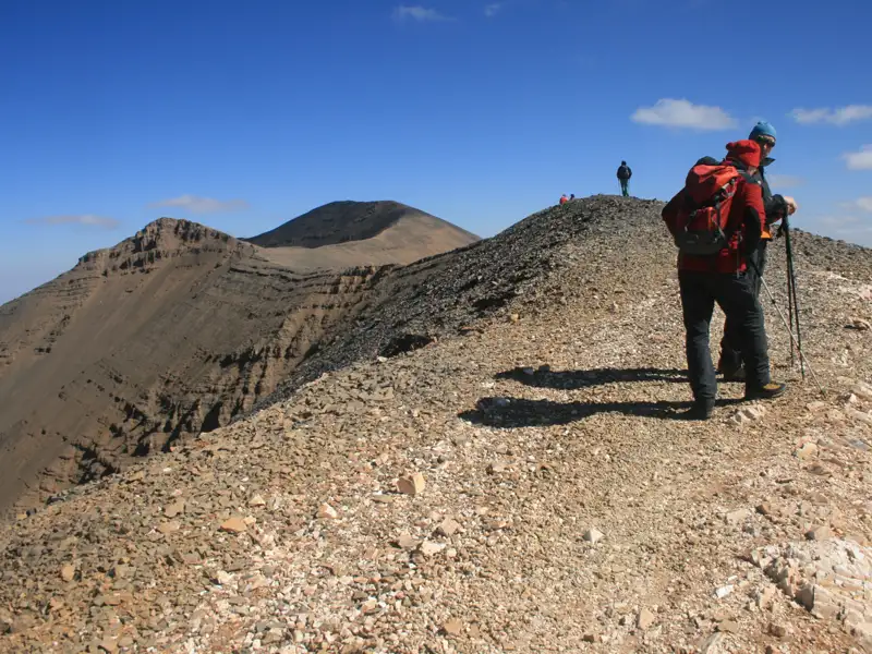 Wanderer auf einem felsigen Bergkamm mit Blick auf weitere Gipfel.