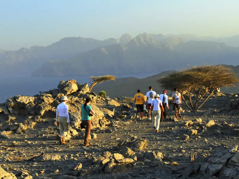 Wandergruppe auf einem felsigen Bergpfad mit Blick auf eine Bergkette und das Meer.