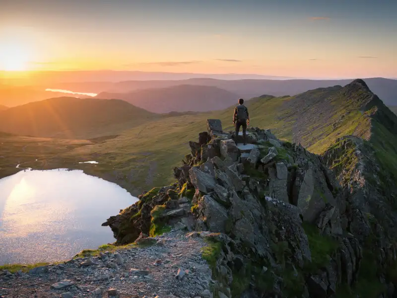 Wanderer auf einem Berggipfel mit Blick auf den Sonnenuntergang und einen See.