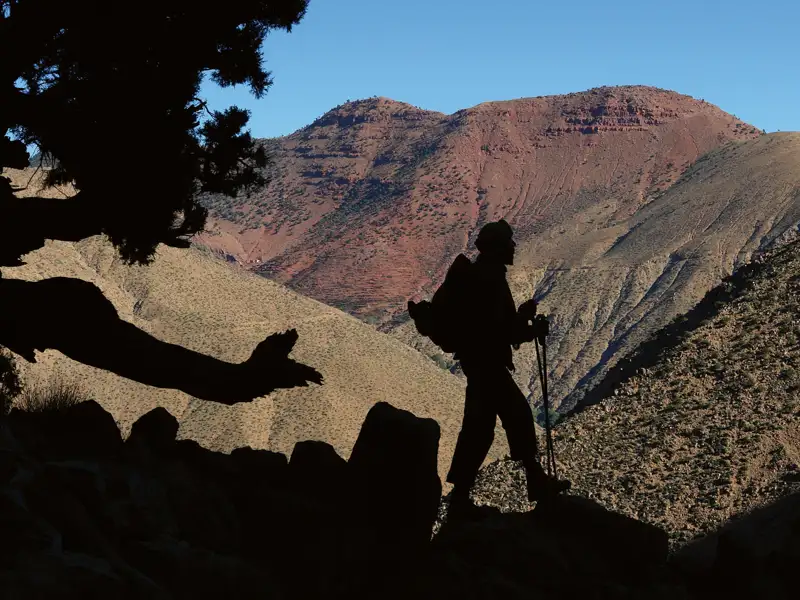 Silhouette eines Wanderers mit Rucksack und Wanderstöcken in einer bergigen Landschaft.