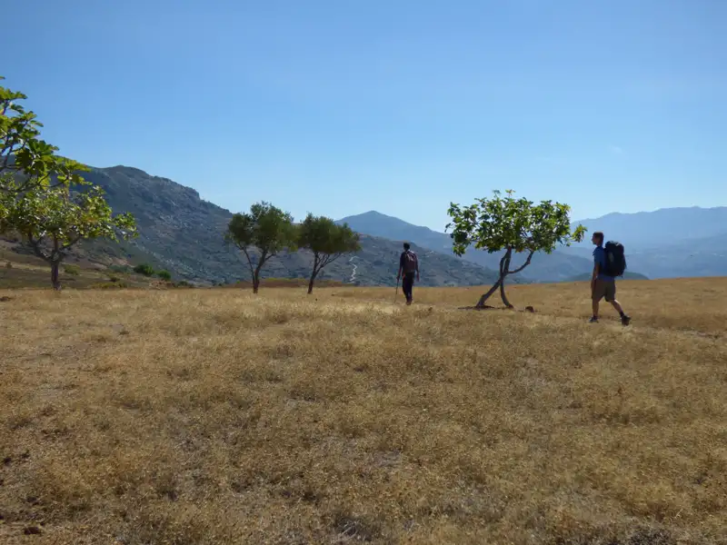 Zwei Wanderer mit Rucksäcken auf einer Wanderung durch eine trockene Landschaft.