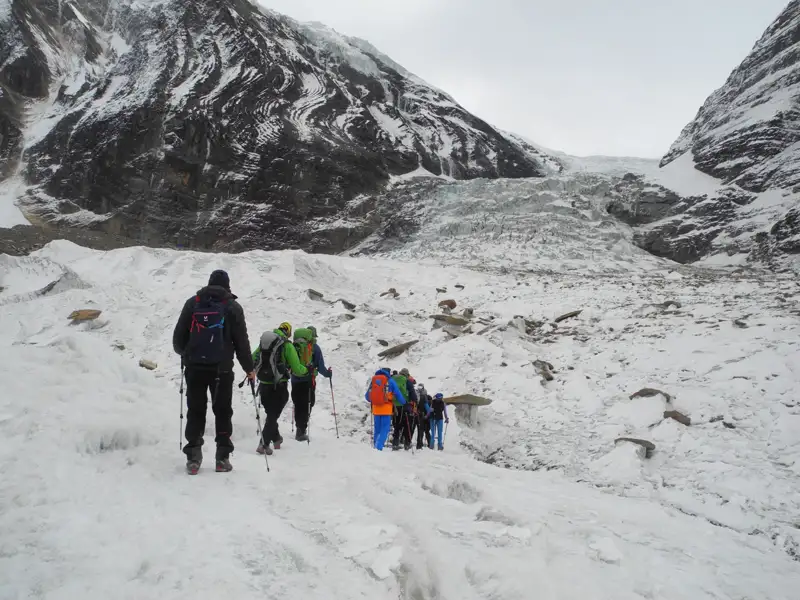 Wanderer mit Rucksäcken und Wanderstöcken überqueren einen Gletscher.