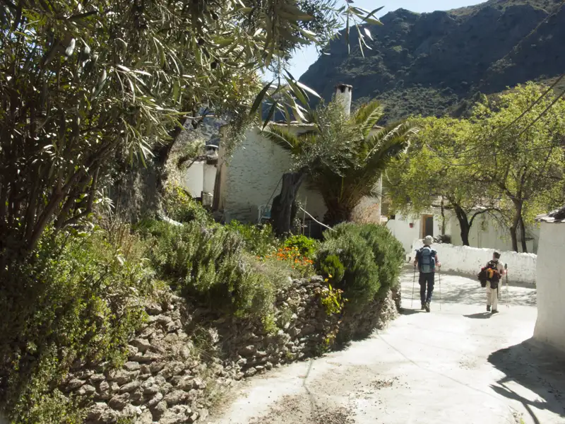 Wanderer auf einem Dorfweg mit Bergkulisse.
