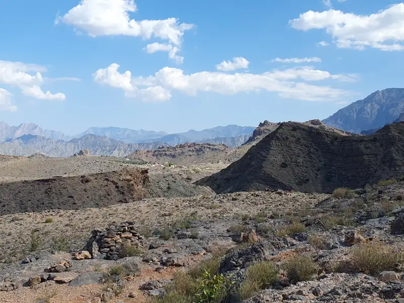 Felsige Berglandschaft mit spärlicher Vegetation und Blick auf weitere Berge im Hintergrund.