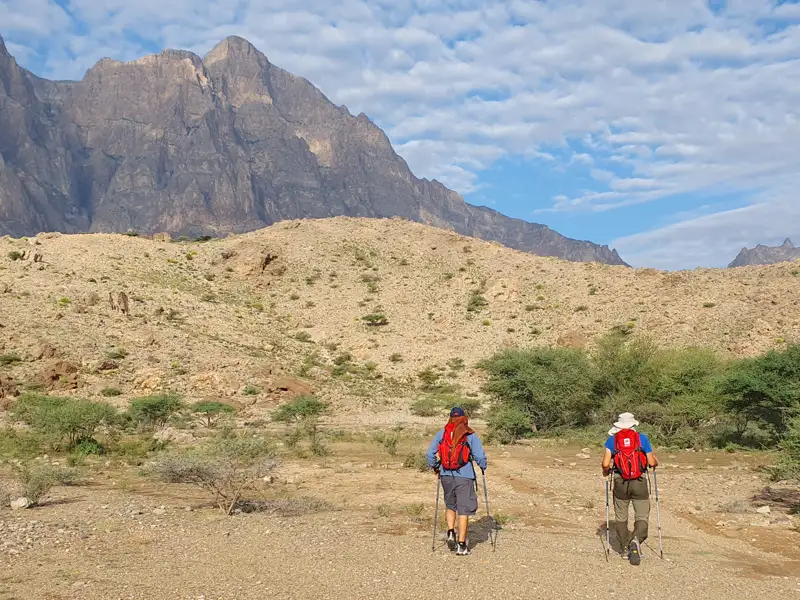 Zwei Wanderer auf einer Trekkingtour in einer bergigen Wüstenlandschaft.