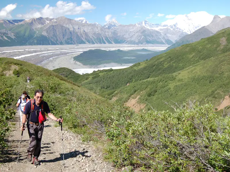 Wanderer auf einem Bergpfad mit Blick auf einen Gletscher und schneebedeckte Berge im Hintergrund.