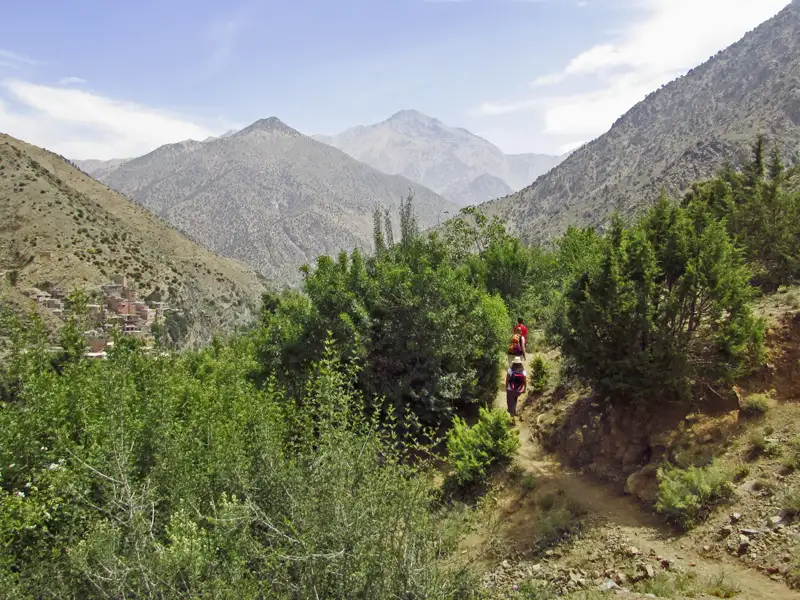 Wanderer auf einem Bergpfad im Atlasgebirge, mit Blick auf ein traditionelles Bergdorf und die umliegende Berglandschaft.
