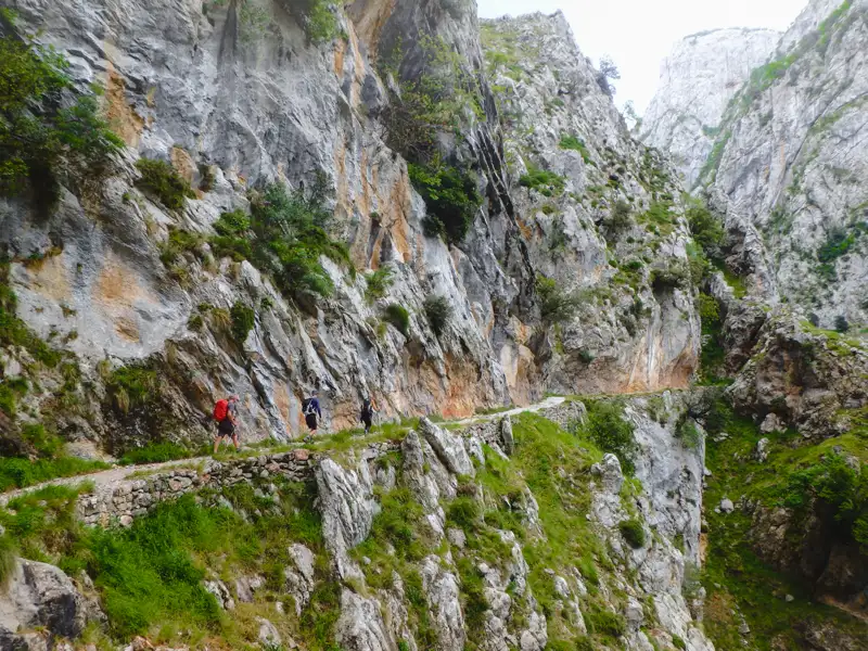 Wanderer auf einem schmalen Bergpfad in einer Schlucht.