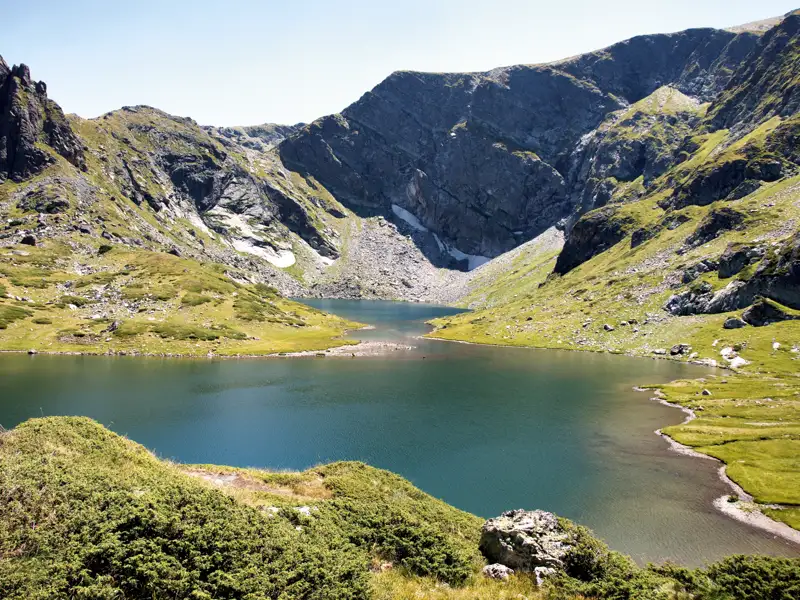 Bergsee mit umliegenden grünen Hängen und felsigen Gipfeln.