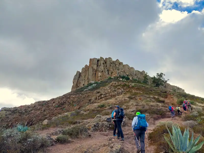 Wandergruppe auf einem Pfad in Richtung einer felsigen Bergformation.