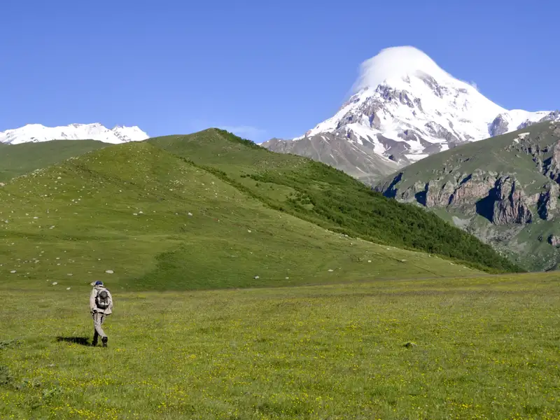 Wanderer in einer Berglandschaft mit schneebedecktem Gipfel im Hintergrund.
