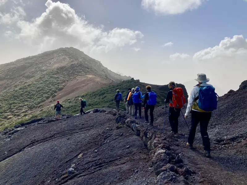 Wandergruppe auf einem Vulkanpfad, umgeben von vulkanischem Gestein und spärlicher Vegetation.