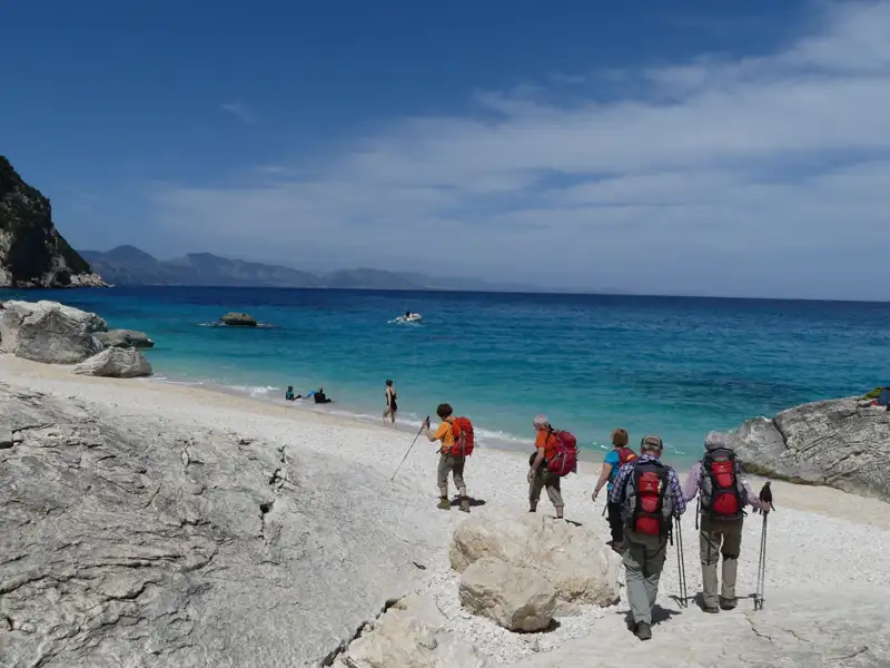 Wanderer erreichen einen weißen Sandstrand am Meer.