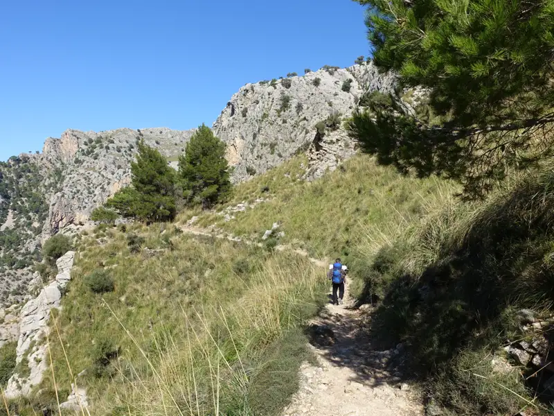 Wanderer auf einem Bergpfad mit felsigen Hängen im Hintergrund.