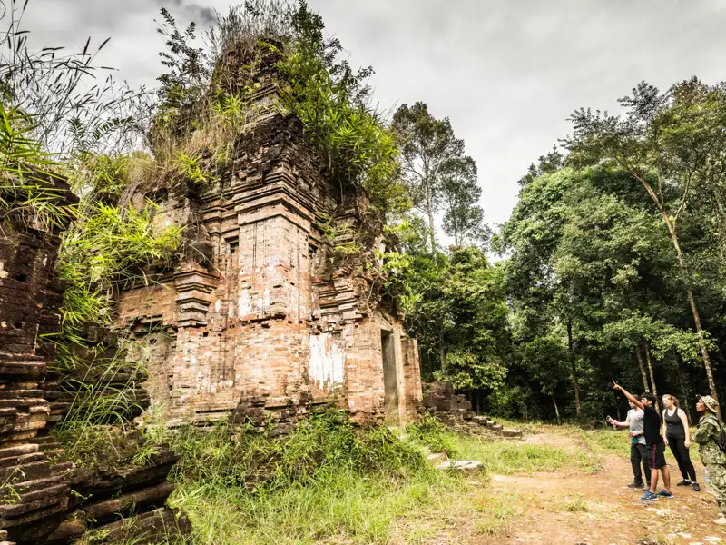 Besichtigung einer alten Tempelruine während einer Reise. Die Ruine zeigt verwitterte Ziegel und üppige Vegetation.