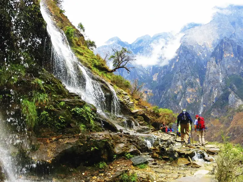 Wanderer auf einem Bergpfad neben einem Wasserfall in den Bergen.