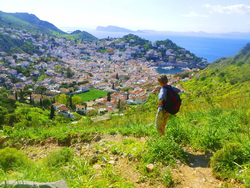 Wanderer auf einem Hügel mit Blick auf eine Küstenstadt und das Meer.