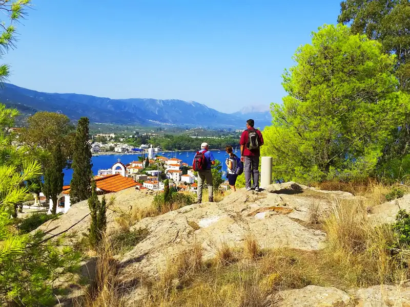 Wanderer auf einem Aussichtspunkt mit Blick auf ein Küstendorf und die umliegende Landschaft.